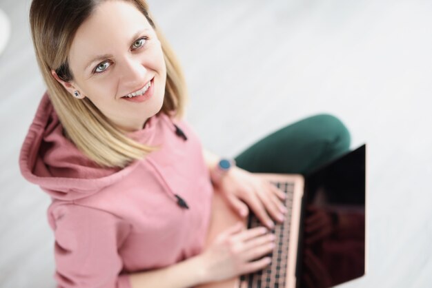 Mulher jovem sentada no chão com o laptop no colo em casa conceito de trabalho remoto on-line