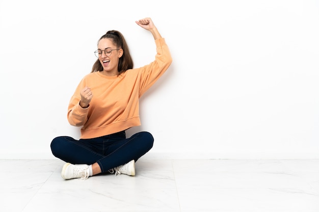 Foto mulher jovem sentada no chão comemorando uma vitória