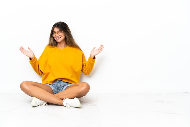 Mulher jovem sentada no chão, isolada no fundo branco, com expressão facial chocada