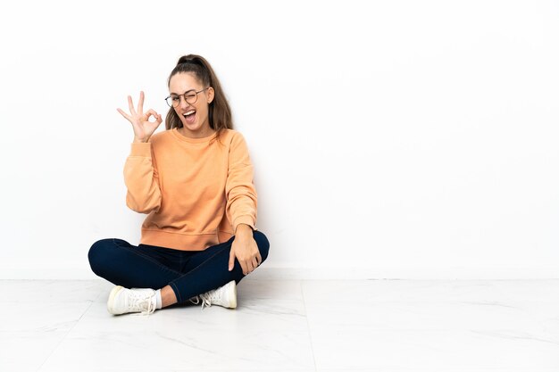 Foto mulher jovem sentada no chão, mostrando sinal de ok com os dedos