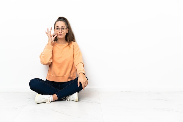 Mulher jovem sentada no chão mostrando um gesto de silêncio