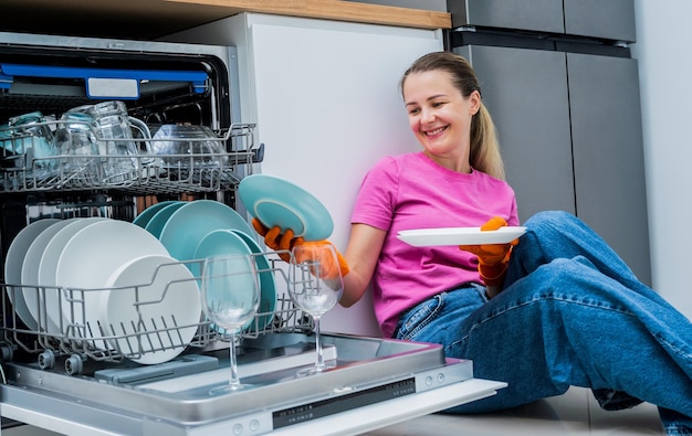 Mulher jovem sentada no chão perto da máquina de lavar pratos