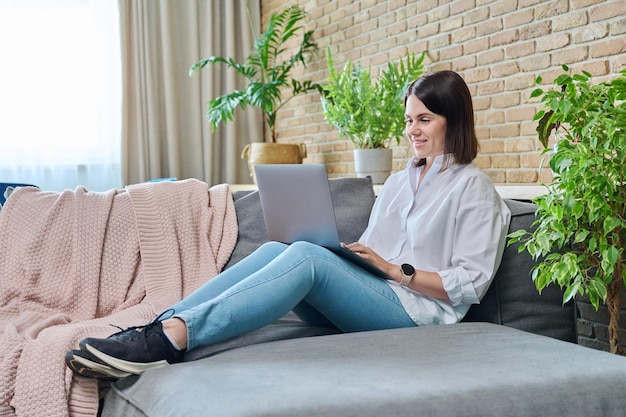 Mulher jovem sentada no sofá usando laptop para trabalho de aprendizagem freelancing