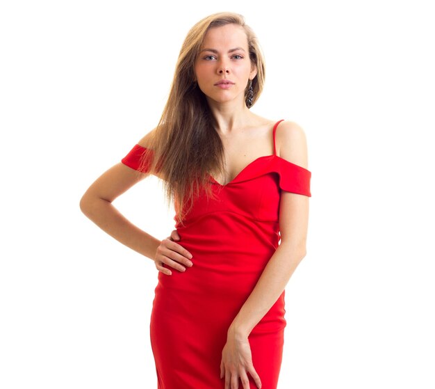 Mulher jovem séria com cabelos castanhos compridos em vestido vermelho acanhado sobre fundo branco no estúdio