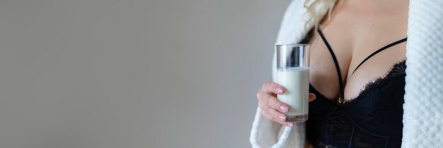 Foto mulher jovem sexy em lingerie preta derramando leite no corpo isolado em cinza