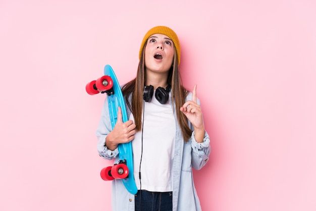 Mulher jovem skatista segurando um skate apontando de cabeça com a boca aberta.