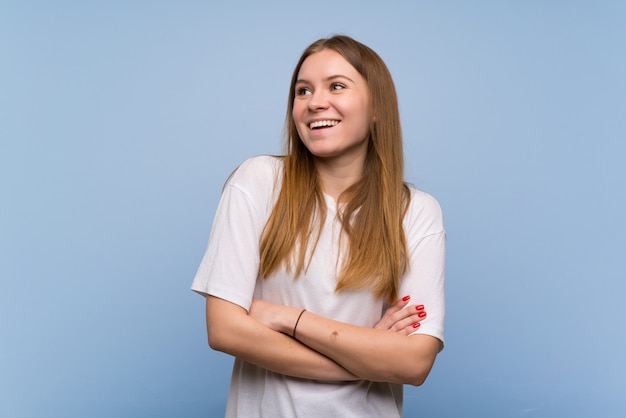 Mulher jovem, sobre, parede azul, mantendo, a, braços cruzaram, enquanto, sorrindo