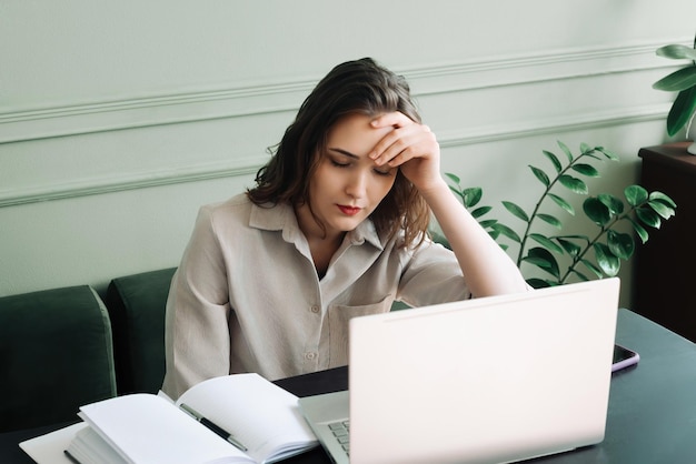Mulher jovem sobrecarregada de trabalho e estressada, a dormir no portátil, perdida nos pensamentos, exausta e estresada.