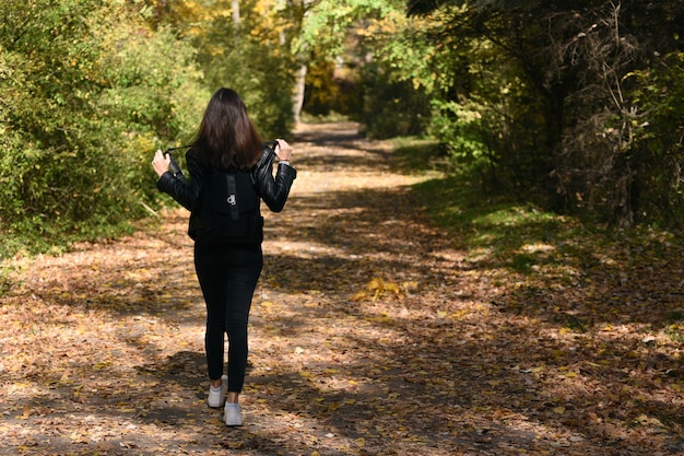 Mulher jovem solitária com cabelo escuro caminha pela floresta. Parque ensolarado de menina ao ar livre. Vista traseira.