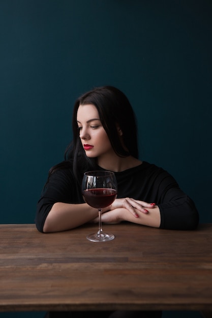 Mulher jovem solitária no bar. Humor melancólico. Mulher triste com vinho tinto sobre fundo azul com espaço livre, encontro romântico malsucedido. Problemas na vida, conceito de tristeza