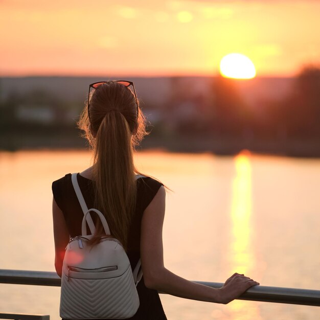 Mulher jovem solitária sozinha na margem do lago desfrutando de bem-estar à noite quente e relaxando no conceito de natureza