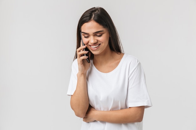 Mulher jovem sorridente casual vestida de pé, isolada no branco, falando no celular