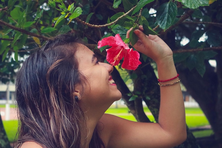 Foto mulher jovem sorridente cheirando flor de hibisco no parque