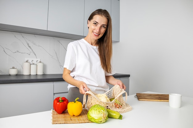 Mulher jovem sorridente, classificando o saco com legumes frescos na cozinha