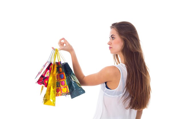 Mulher jovem sorridente com cabelo comprido na blusa branca e saia preta segurando sacolas de compras no estúdio