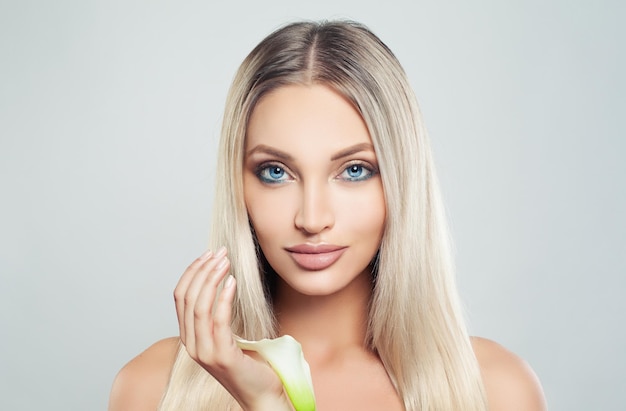 Mulher jovem sorridente com cabelo loiro de pele limpa e fresca e flores de lírio Tratamento facial Cosmetologia beleza cuidados com a pele e spa