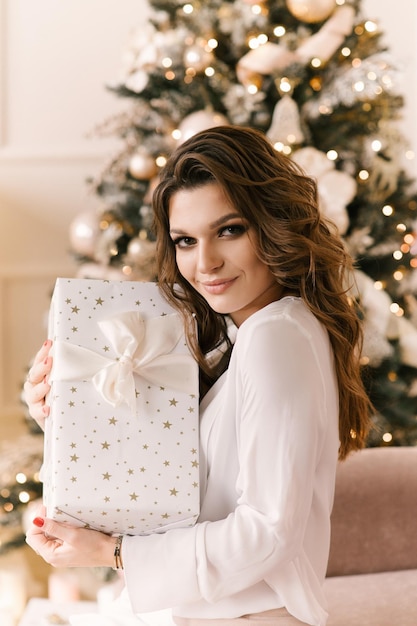 Mulher jovem sorridente com caixa de presente de natal perto da árvore de natal