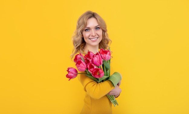 Mulher jovem sorridente com flores de tulipa de primavera em fundo amarelo