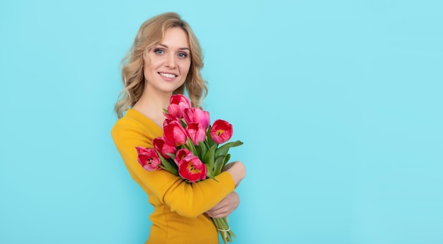 Mulher jovem sorridente com flores de tulipa de primavera no dia da mulher de fundo azul