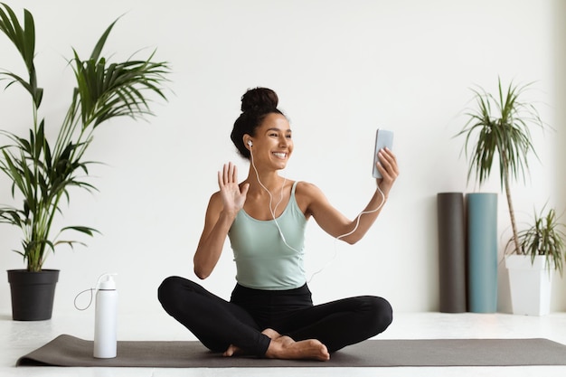 Mulher jovem sorridente com smartphone fazendo videochamada com sofá de ioga