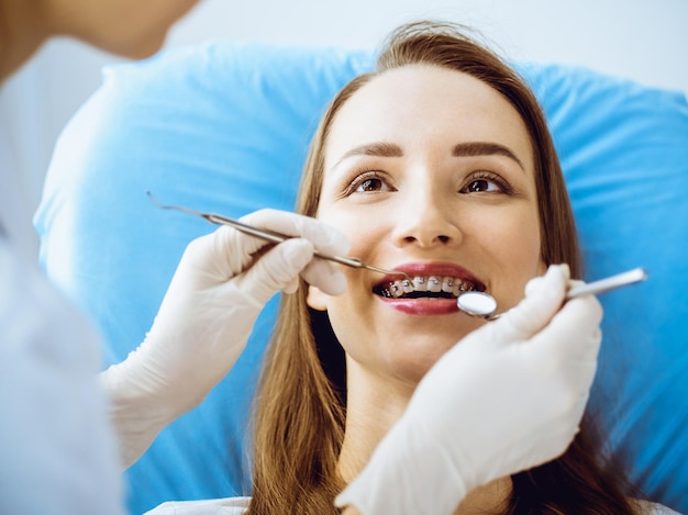 Foto mulher jovem sorridente com suportes ortodônticos examinados pelo dentista na clínica odontológica. dentes saudáveis e conceito de cuidados médicos.