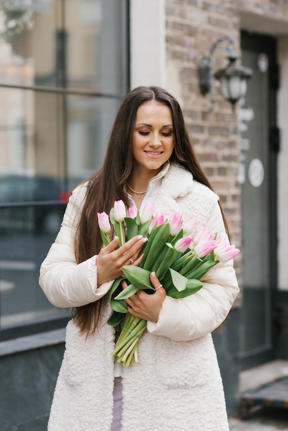 Mulher jovem sorridente com um buquê de tulipas de primavera em uma rua da cidade