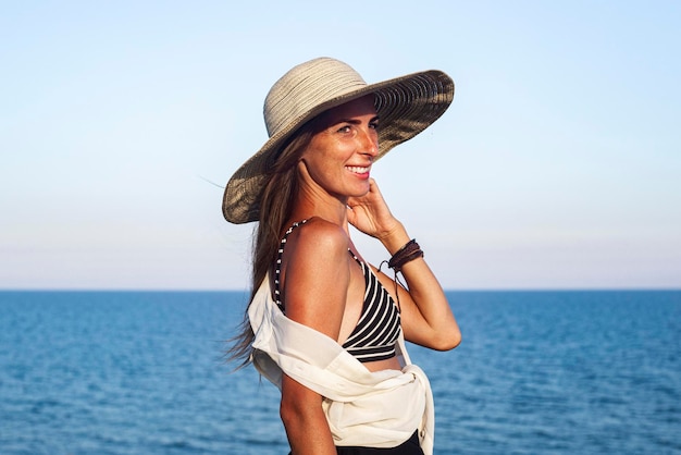 Mulher jovem sorridente com um chapéu no fundo do mar e do céu.