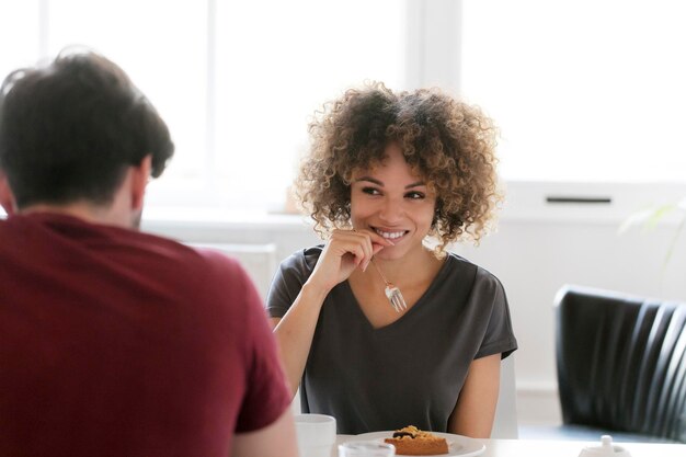 Foto mulher jovem sorridente comendo bolo na mesa olhando para o homem