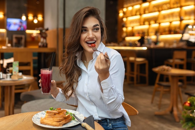 Foto mulher jovem sorridente comer pequeno-almoço almoço pepino torrada sanduíche e beber suco conceito de estilo de vida de dieta saudável