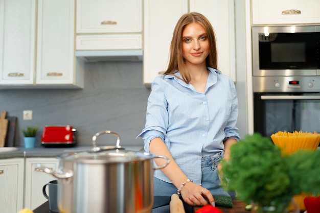 Mulher jovem sorridente cortando legumes para salada na cozinha