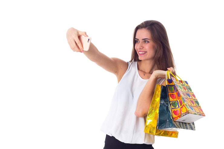 Foto mulher jovem sorridente de blusa branca e saia preta segurando sacolas de compras e usando smartphone rosa