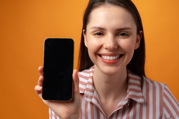 Foto mulher jovem sorridente e feliz mostrando a tela preta do smartphone com espaço de cópia