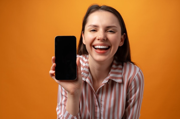 Mulher jovem sorridente e feliz mostrando a tela preta do smartphone com espaço de cópia