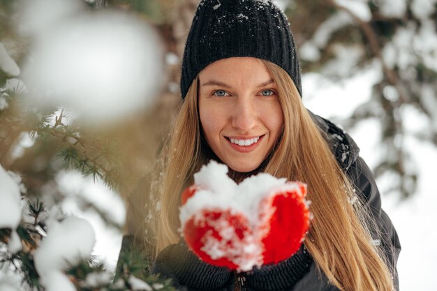 Mulher jovem sorridente e feliz se divertindo com a neve em um parque de inverno