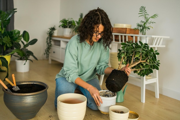 Mulher jovem sorridente e pote com planta trabalho feliz no jardim interno ou escritório doméstico aconchegante com diferentes plantas de casa Jardineira ou florista milenar feliz cuidando de flores domésticas