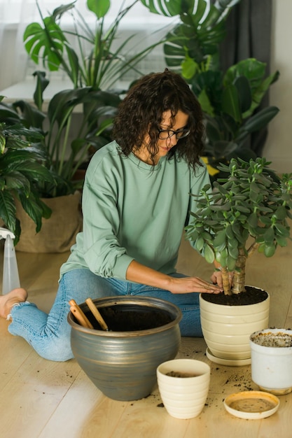 Mulher jovem sorridente e pote com planta trabalho feliz no jardim interno ou escritório doméstico aconchegante com diferentes plantas de casa Jardineira ou florista milenar feliz cuidando de flores domésticas