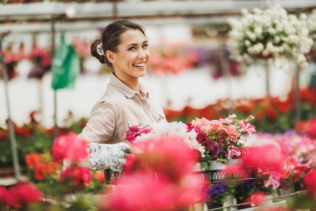 Mulher jovem sorridente ela segurando a caixa com lindas flores em um centro de jardim ou viveiro de plantas.