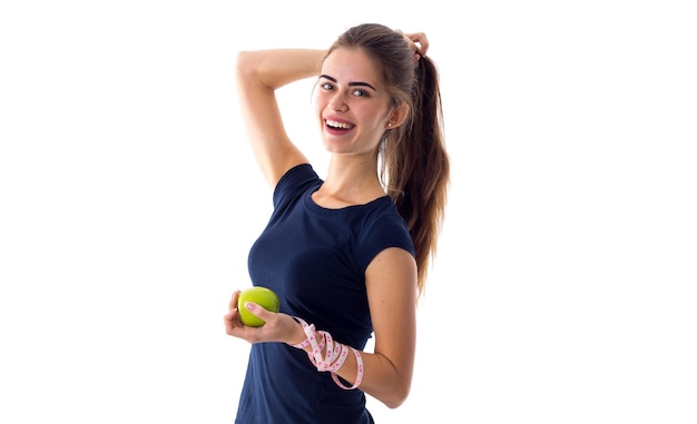 Mulher jovem sorridente em camiseta azul com centímetro em volta do pescoço segurando maçã verde na mão sobre fundo branco no estúdio