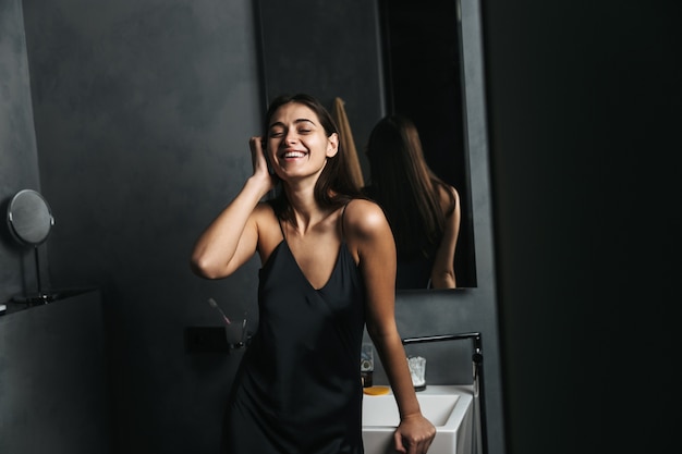 Mulher jovem sorridente em pé no espelho do banheiro pela manhã
