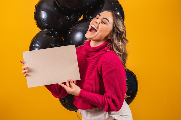 Mulher jovem sorridente encantadora com banner com espaço livre para texto e balões em fundo preto. Conceito de promoção Black Friday