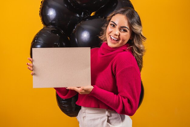 Mulher jovem sorridente encantadora com banner com espaço livre para texto e balões em fundo preto. Conceito de promoção Black Friday