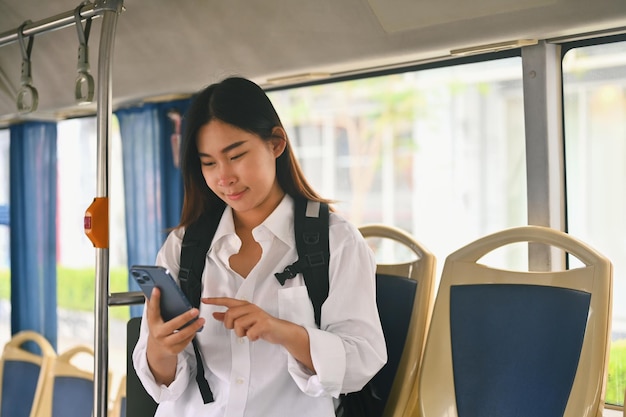 Mulher jovem sorridente enviando mensagens de texto no smartphone enquanto viaja de ônibus Conceito de transporte público