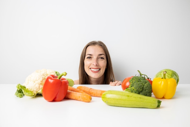 Mulher jovem sorridente espreitando debaixo da mesa olhando legumes frescos