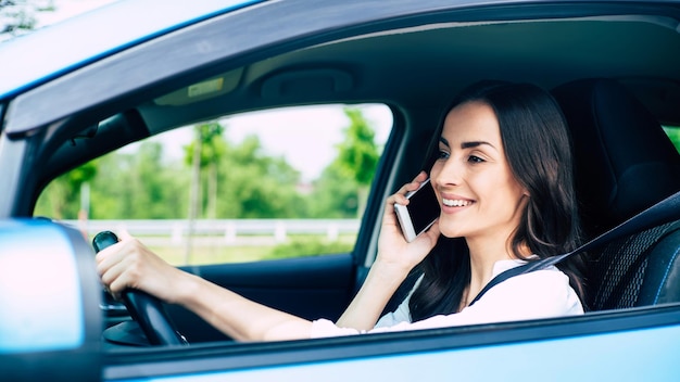 Mulher jovem sorridente falando ao telefone enquanto dirige um carro