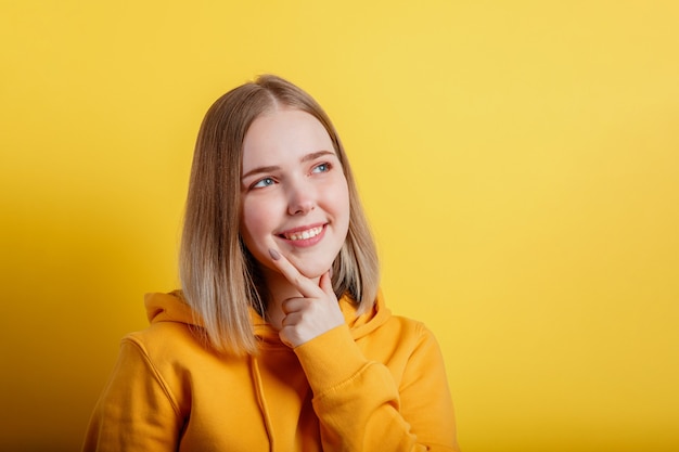 Mulher jovem sorridente feliz pensa o pensamento. Retrato de adolescente emocional olhando no pensamento profundo do espaço vazio sobre a ideia ou pergunta positiva sobre fundo de cor amarela com espaço de cópia.