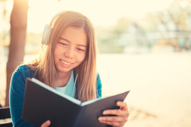 Mulher jovem sorridente lendo um livro sentada em um banco ao ar livre