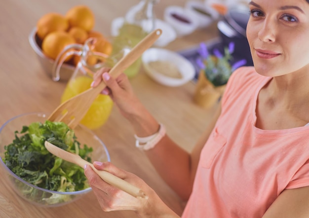 Foto mulher jovem sorridente misturando salada fresca na cozinha