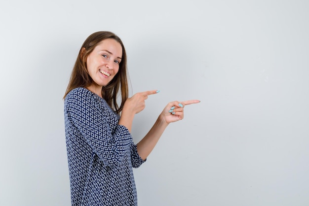 Mulher jovem sorridente mostrando a direita com os dedos no fundo branco