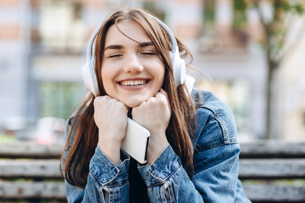 Mulher jovem, sorridente, ouvindo música com fones de ouvido. Garota ouvindo músicas através de fones de ouvido sem fio. Closeup rosto de adolescente.