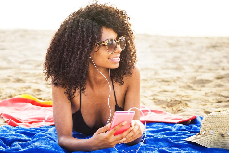 Foto mulher jovem sorridente ouvindo música enquanto deitada na praia